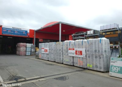Abri avec une toile tendue rouge, et qui protège la sortie caisse du Brico Dépôt.