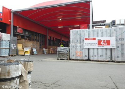 Abri avec une toile tendue rouge, et destiné à protéger les matériaux exposés à l'extérieur du magasin Brico Dépôt.