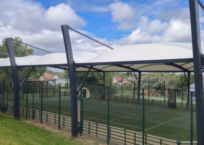Vue sur la charpente métallique grise et la toile tendue blanche de l'abri du terrain multisport d'Etting.