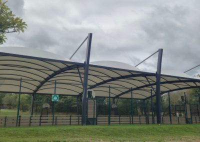 Abri du terrain multisport avec une toile tendue blanche et une structure métallique grise.
