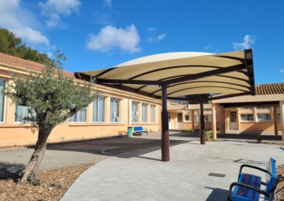 Vue sur l'école et le préau dont la toile tendue est de couleur ivoire.