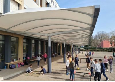 Vue sur le nouveau préau de l'école Paul Fabre dont la toile tendue est blanche, et les enfants jouant dessous.