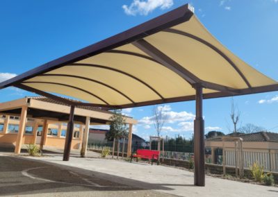 Vue de sous le préau de l'école dont la toile tendue a un colori ivoire.