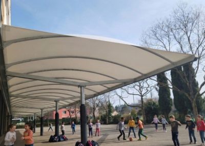 Vue sur le préau dont la toile tendue est blanche et les poteaux ronds entourés de protections en mousse.