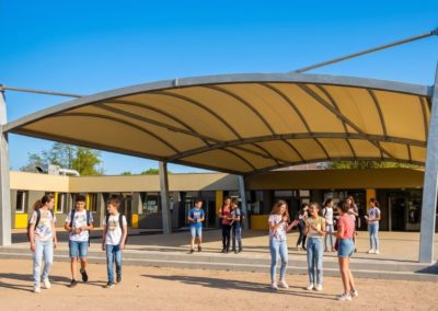 Collégiens qui discutent debout à côté et sous le préau avec une toile tendue beige.